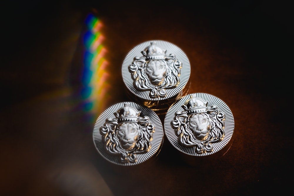 três botões de cabeça de leão de prata sentados em uma mesa
