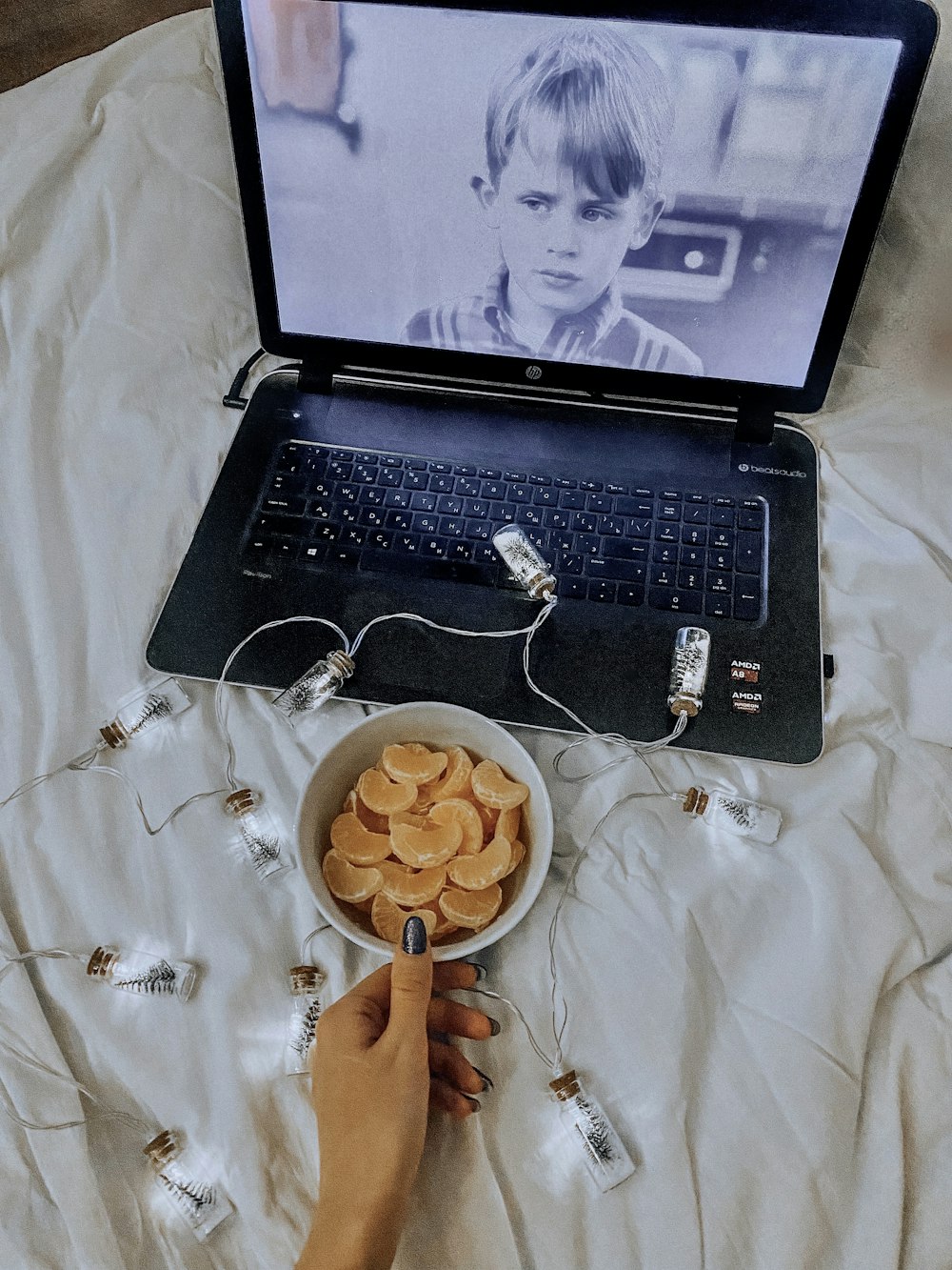 Una persona que usa una computadora portátil en una cama con un tazón de papas fritas