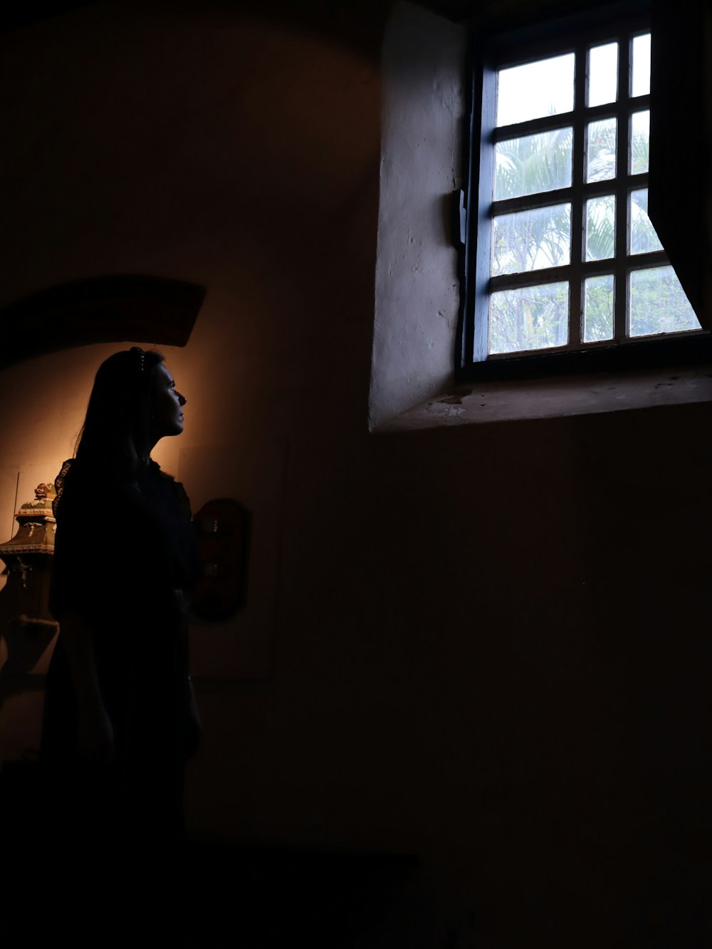 Une femme debout devant une fenêtre dans une pièce sombre