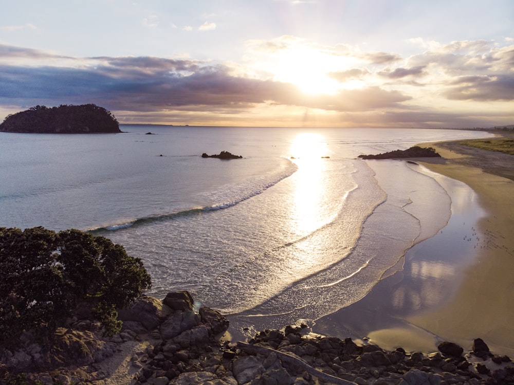 the sun is setting over the ocean with a beach in the foreground