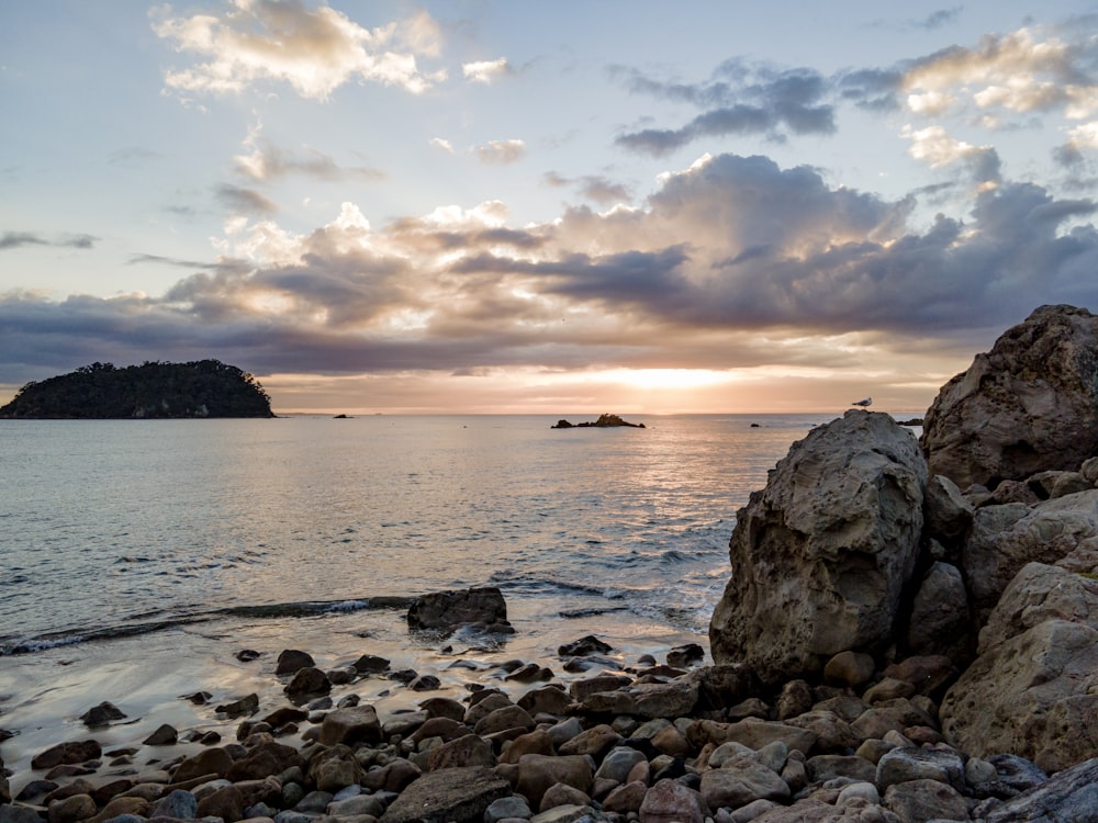 the sun is setting over a rocky beach