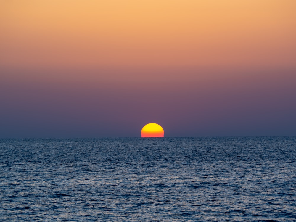 a sunset over the ocean with a boat in the distance
