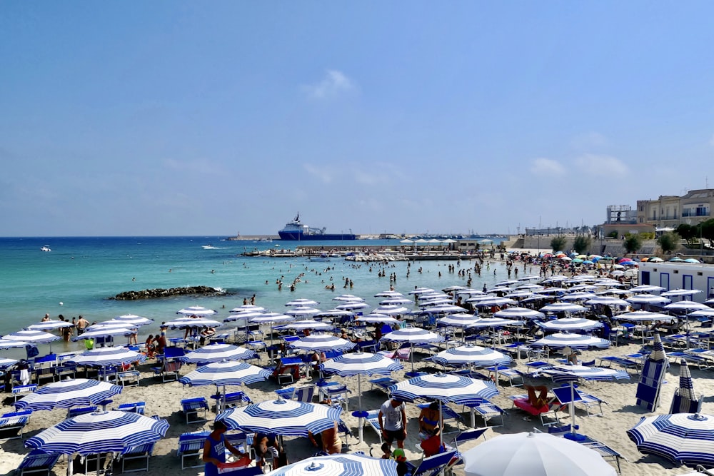 a crowded beach with blue and white umbrellas