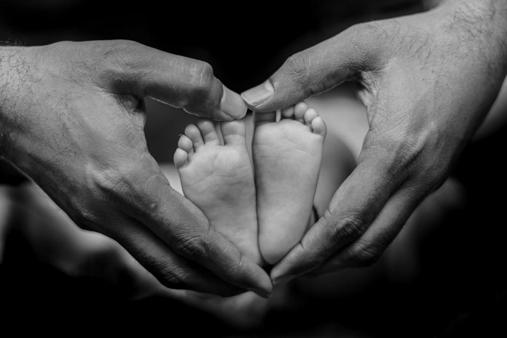 a black and white photo of two hands holding a baby's feet