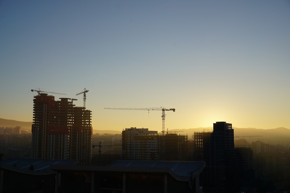 a sunset view of a city with cranes in the background