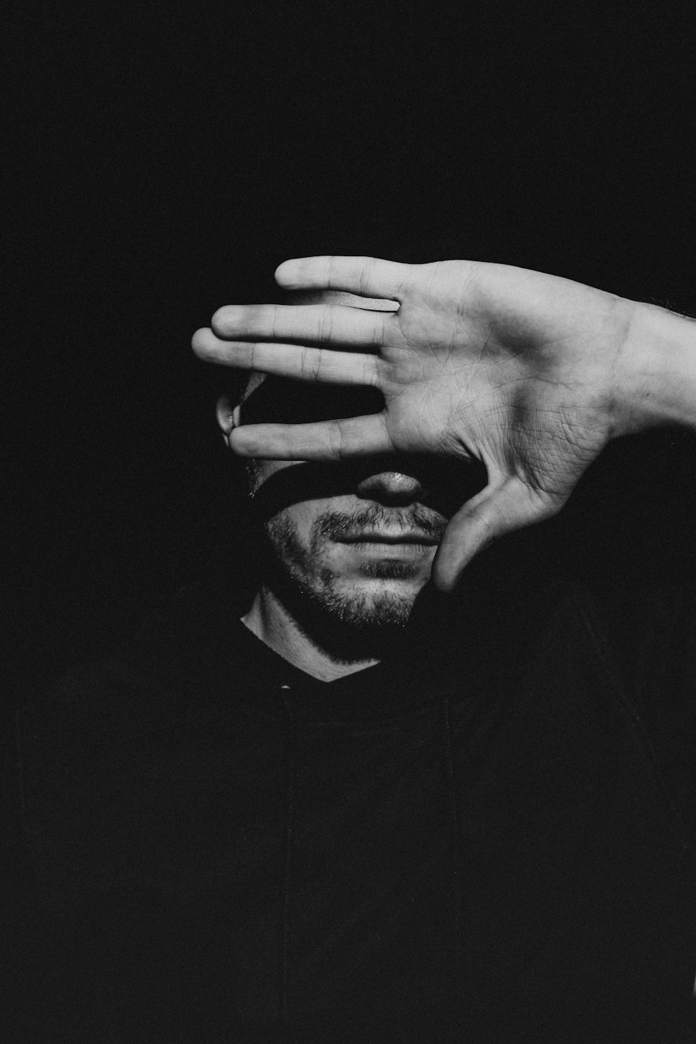 a black and white photo of a man covering his eyes