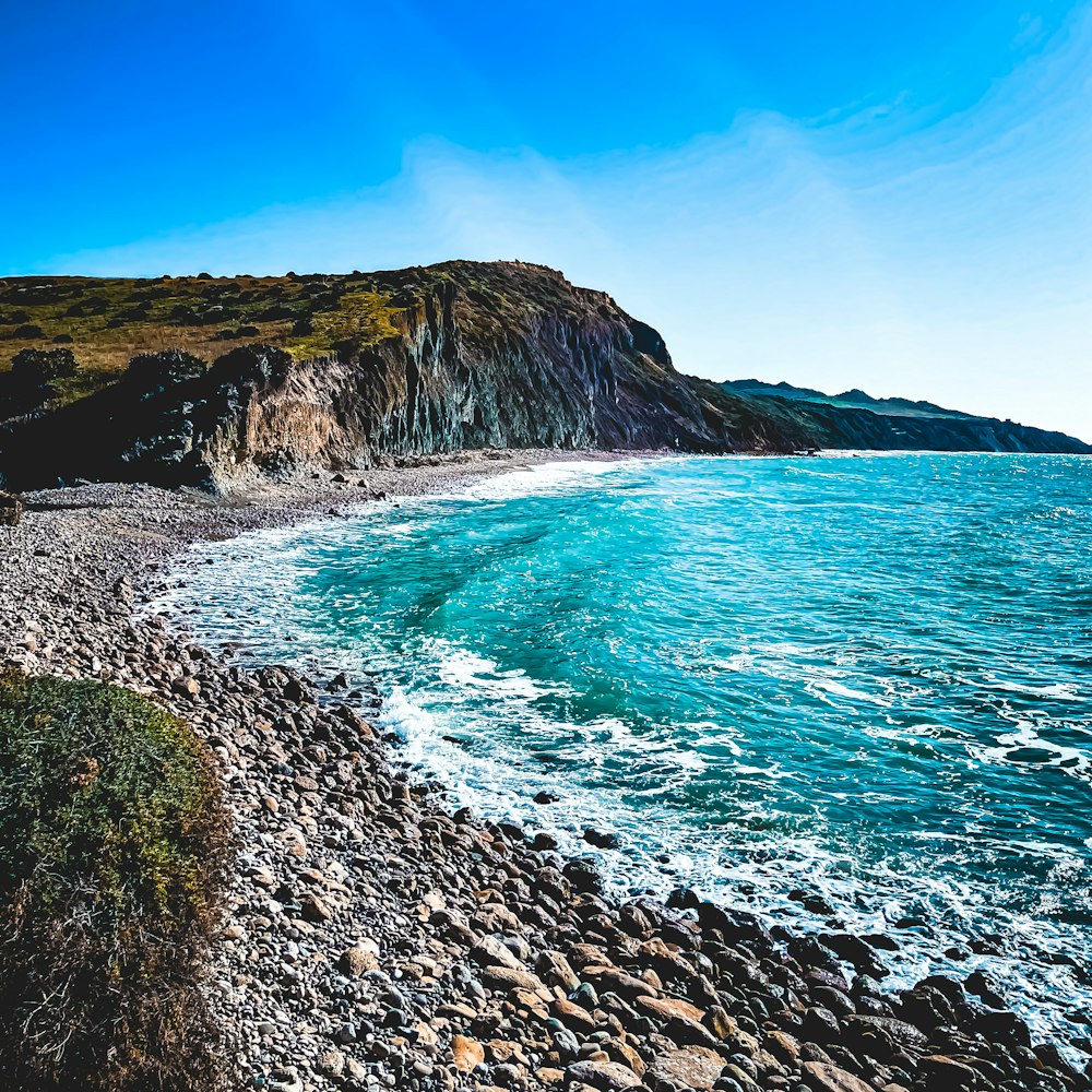 a rocky beach next to the ocean under a blue sky
