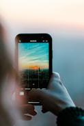 Close-up of a smartphone capturing a sunset over a city skyline.