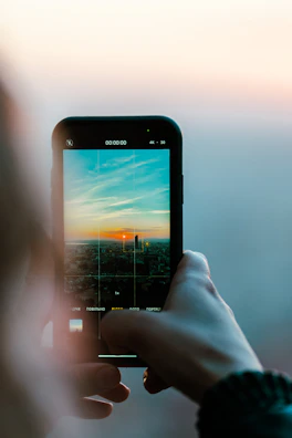 Person holding a smartphone outdoors with a cityscape behind.