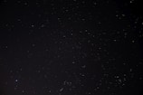 A vast, dark night sky is dotted with countless tiny, twinkling stars of varying brightness, suggesting a clear and expansive view of the cosmos.