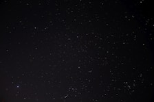 A vast, dark night sky is dotted with countless tiny, twinkling stars of varying brightness, suggesting a clear and expansive view of the cosmos.