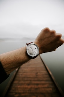 a man's hand holding onto a watch on a dock