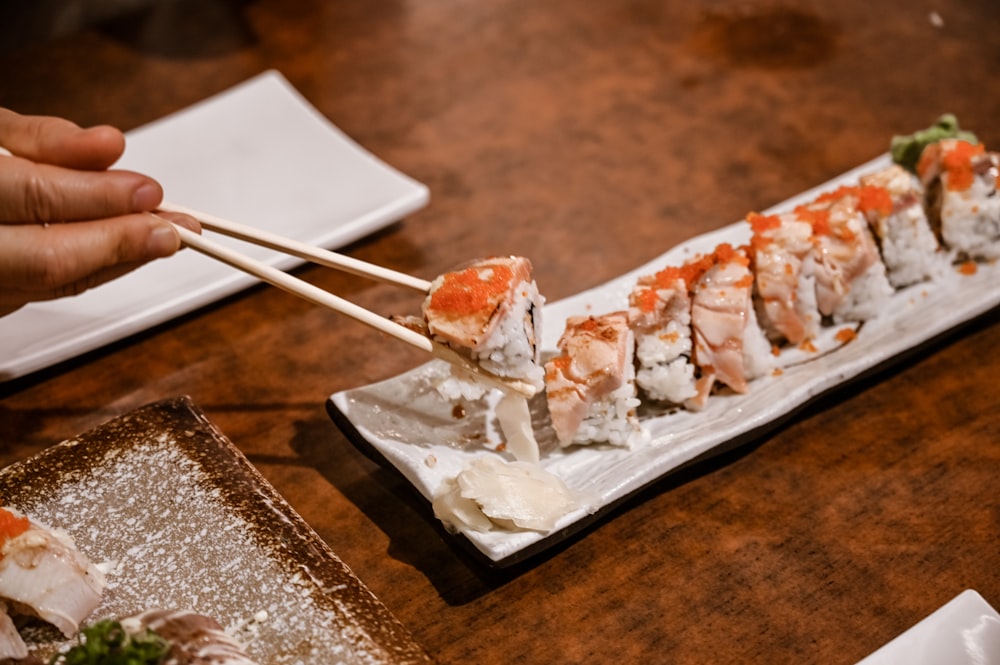 a person holding chopsticks over a plate of sushi