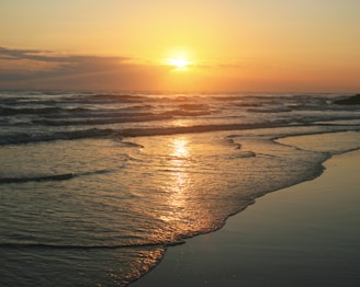 the sun is setting over the water at the beach