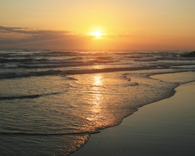 the sun is setting over the water at the beach
