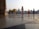 People are walking near a prominent religious structure with golden domes in the background. The ground is made of smooth marble tiles, giving a reflective effect. Several individuals are dressed in traditional attire, including one person wearing a bright orange robe and others donning turbans.
