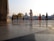 People are walking near a prominent religious structure with golden domes in the background. The ground is made of smooth marble tiles, giving a reflective effect. Several individuals are dressed in traditional attire, including one person wearing a bright orange robe and others donning turbans.