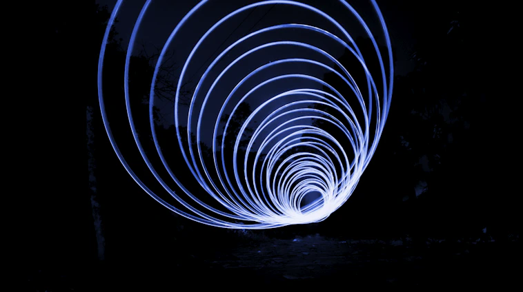 Abstract glowing circular lens with electric-blue light trails sweeping over a dark horizon.