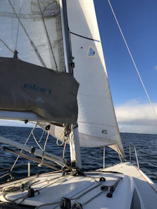 A sleek sailing boat cutting through calm blue waters under a clear sky.