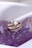 A gold ring with a triangular white centerpiece and small gemstones set in a curve rests on a purple crystalline surface.