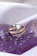 A gold ring with a triangular white centerpiece and small gemstones set in a curve rests on a purple crystalline surface.