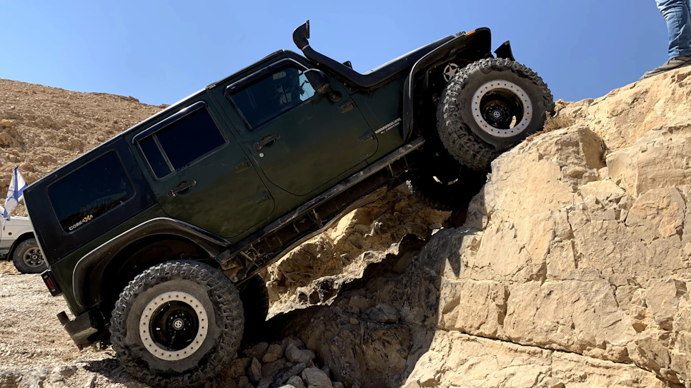 A vibrant yellow and black side-by-side with big tires climbing a muddy rock trail under a bright blue sky.