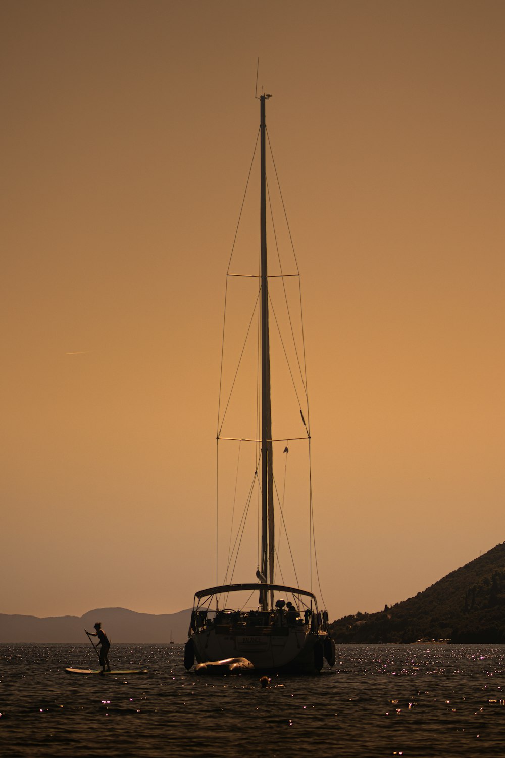 a person standing on a surfboard in the water near a sailboat