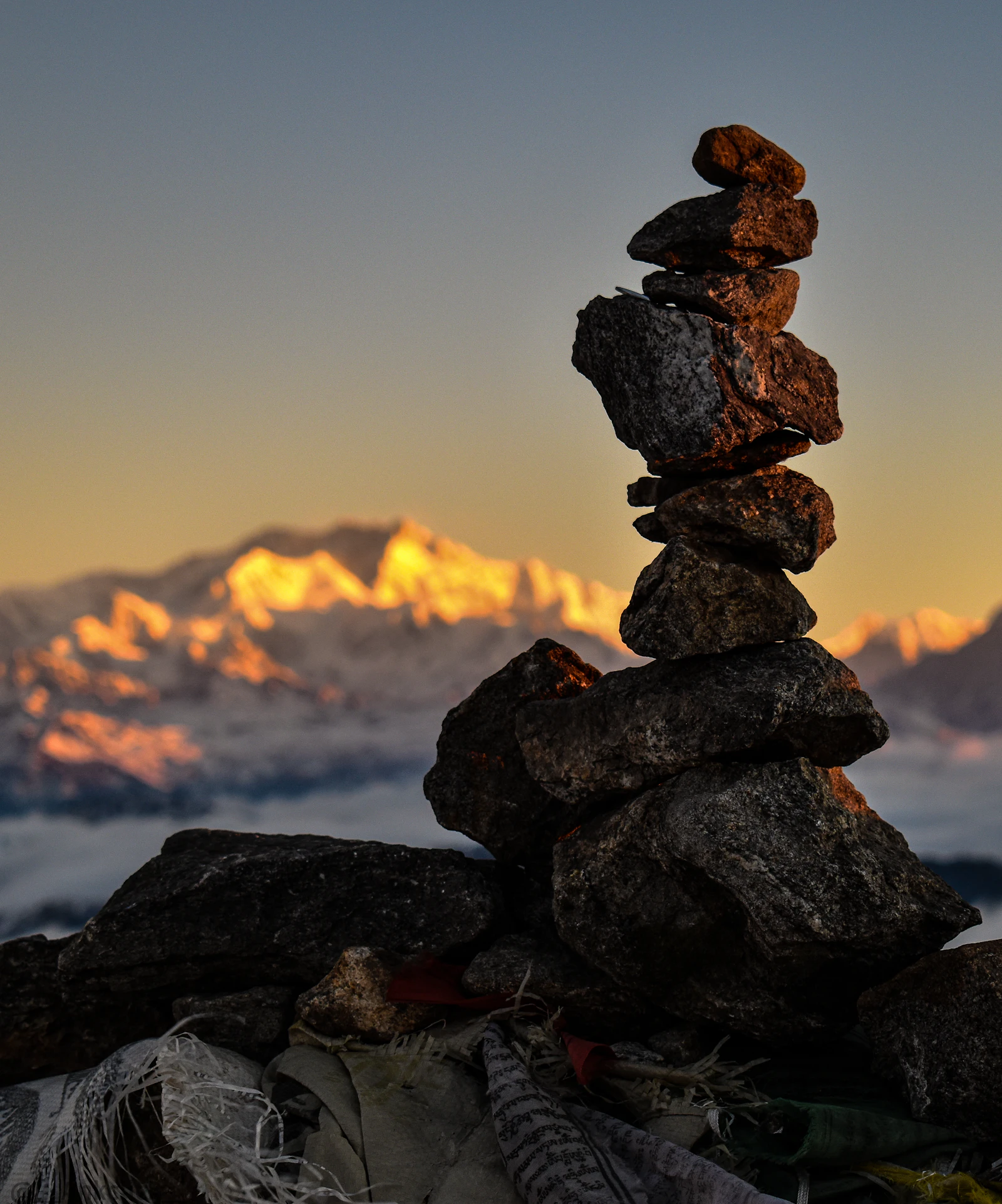 A stone cairn at Sandakphu at sunrise, with the Kanchenjunga massif lit gold above a sea of cloud