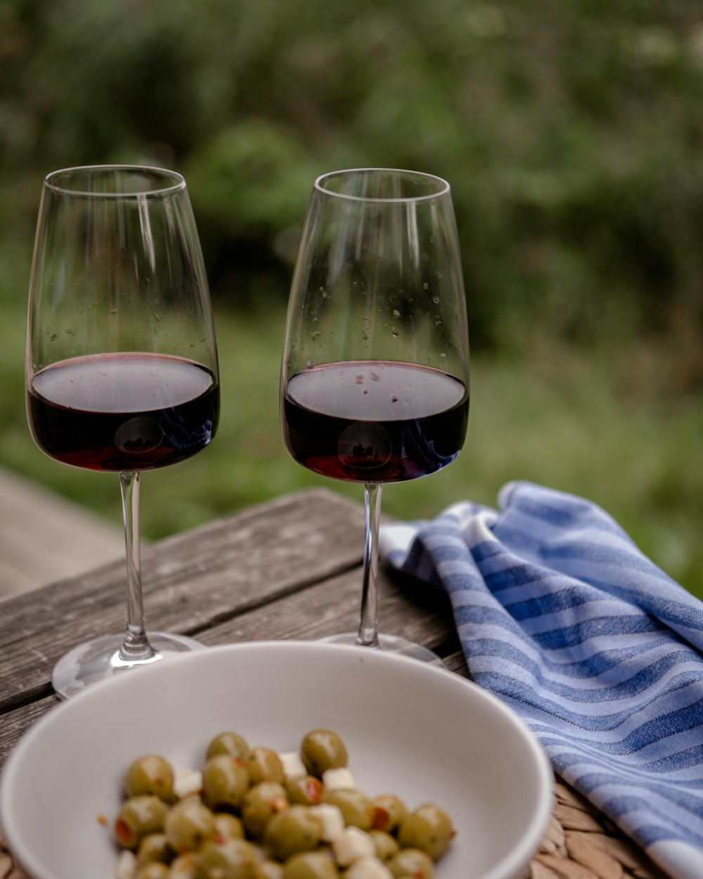 two glasses of red wine and a plate of green olives