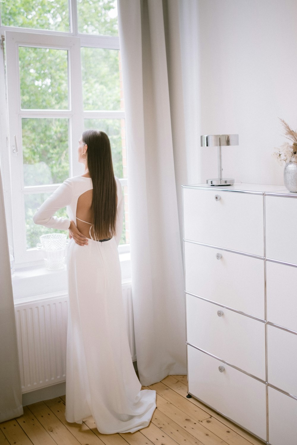 a woman in a white dress looking out a window