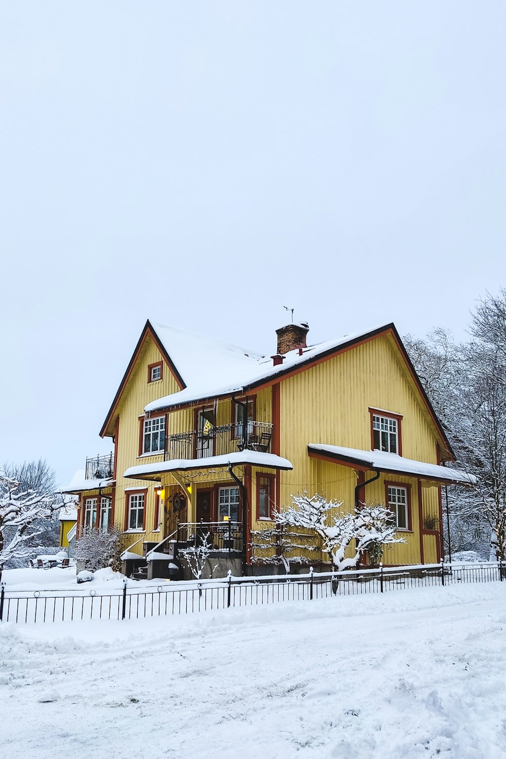 ein großes gelbes Haus mit Schnee bedeckt neben einem Zaun