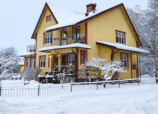 a large yellow house covered in snow next to a fence