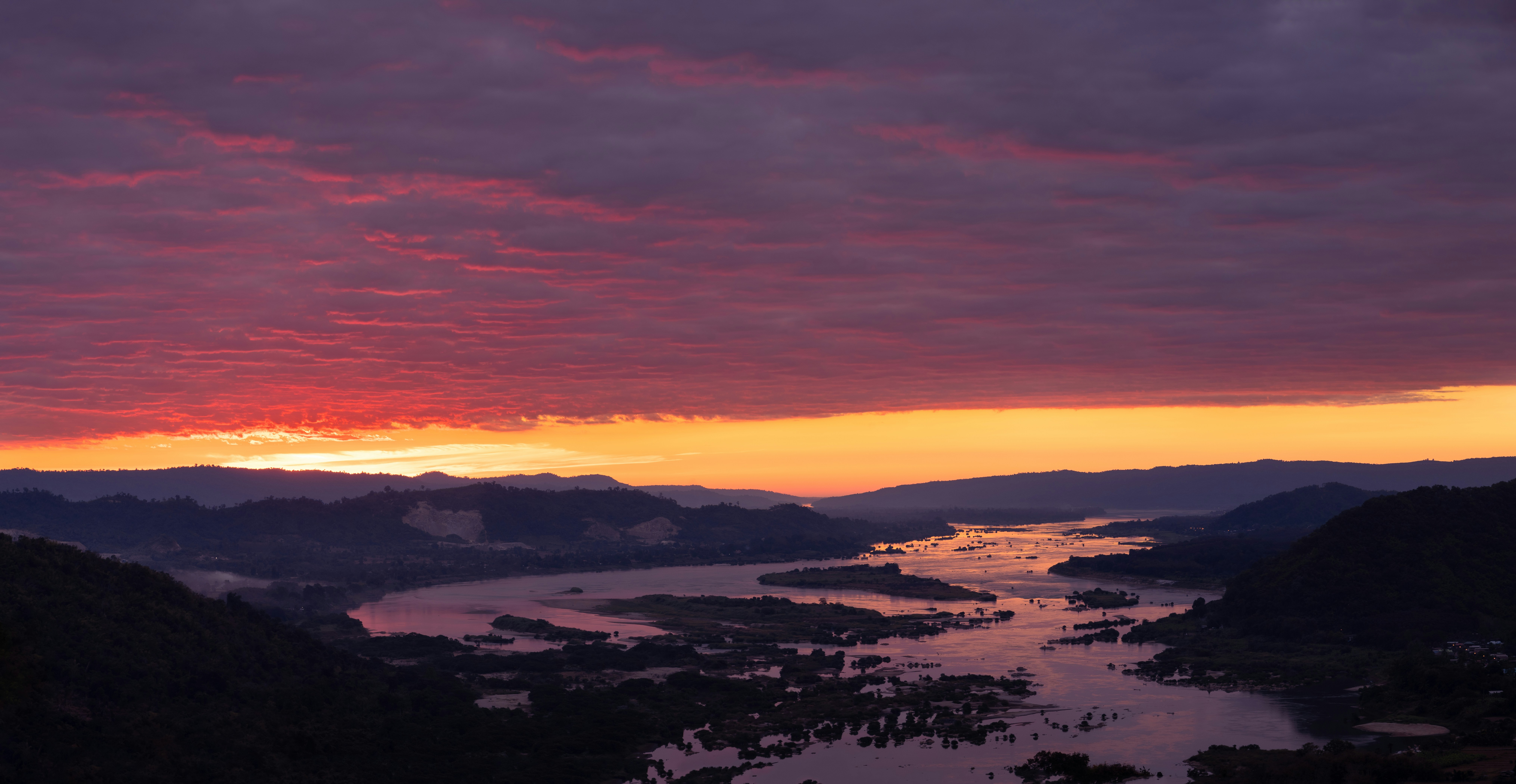 a sunset over a river with mountains in the background
