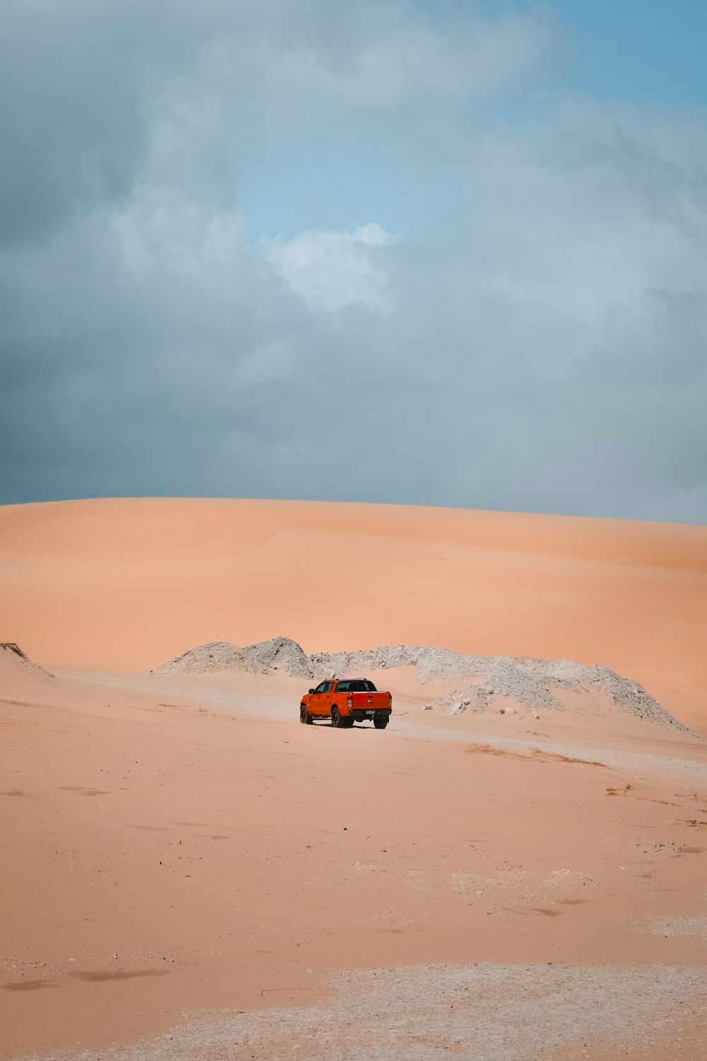 a red truck driving through a desert under a cloudy sky