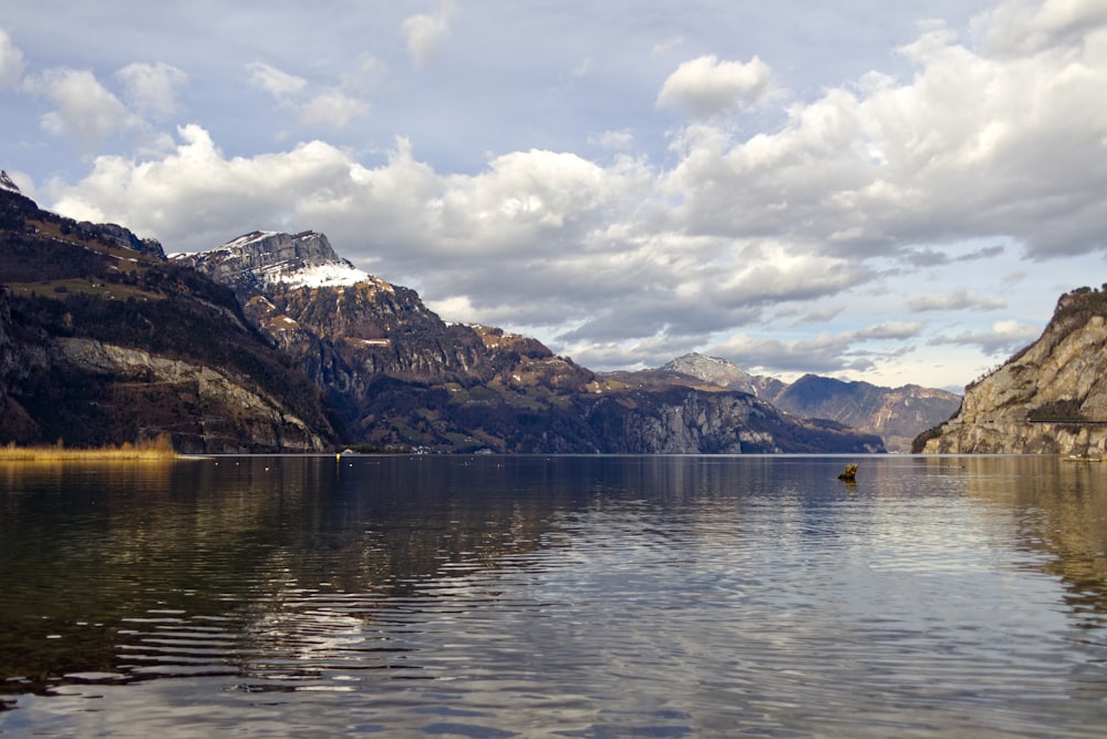 a body of water surrounded by mountains under a cloudy sky