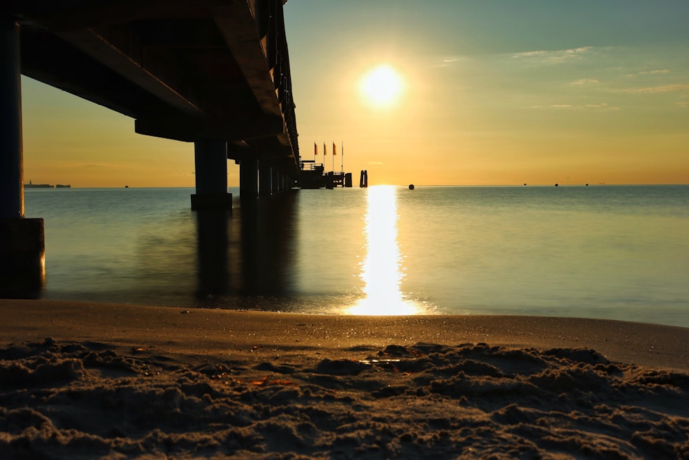 the sun is setting over the water under a bridge