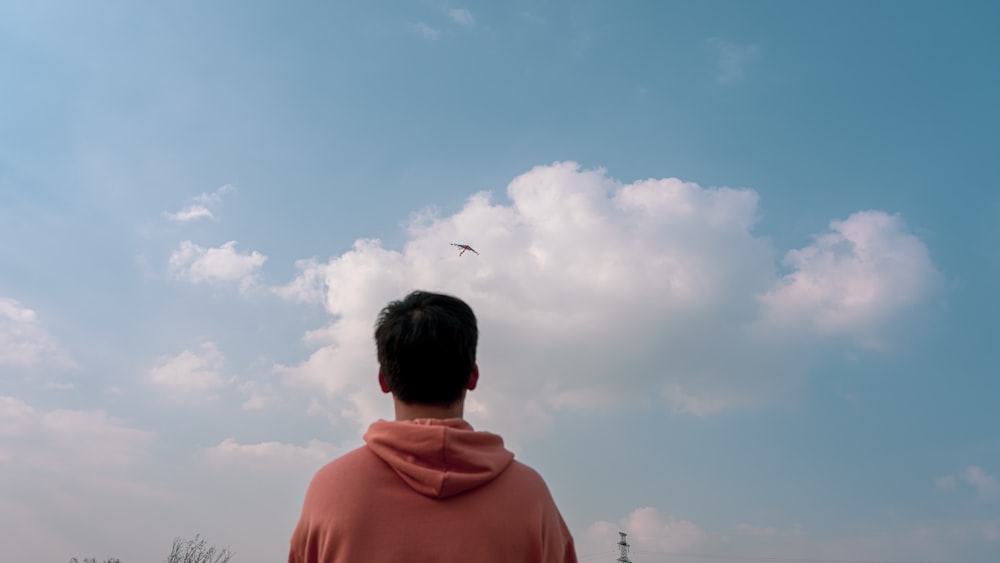 a man in a hoodie looking up at a bird in the sky