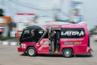 a pink bus driving down a street next to a tall building