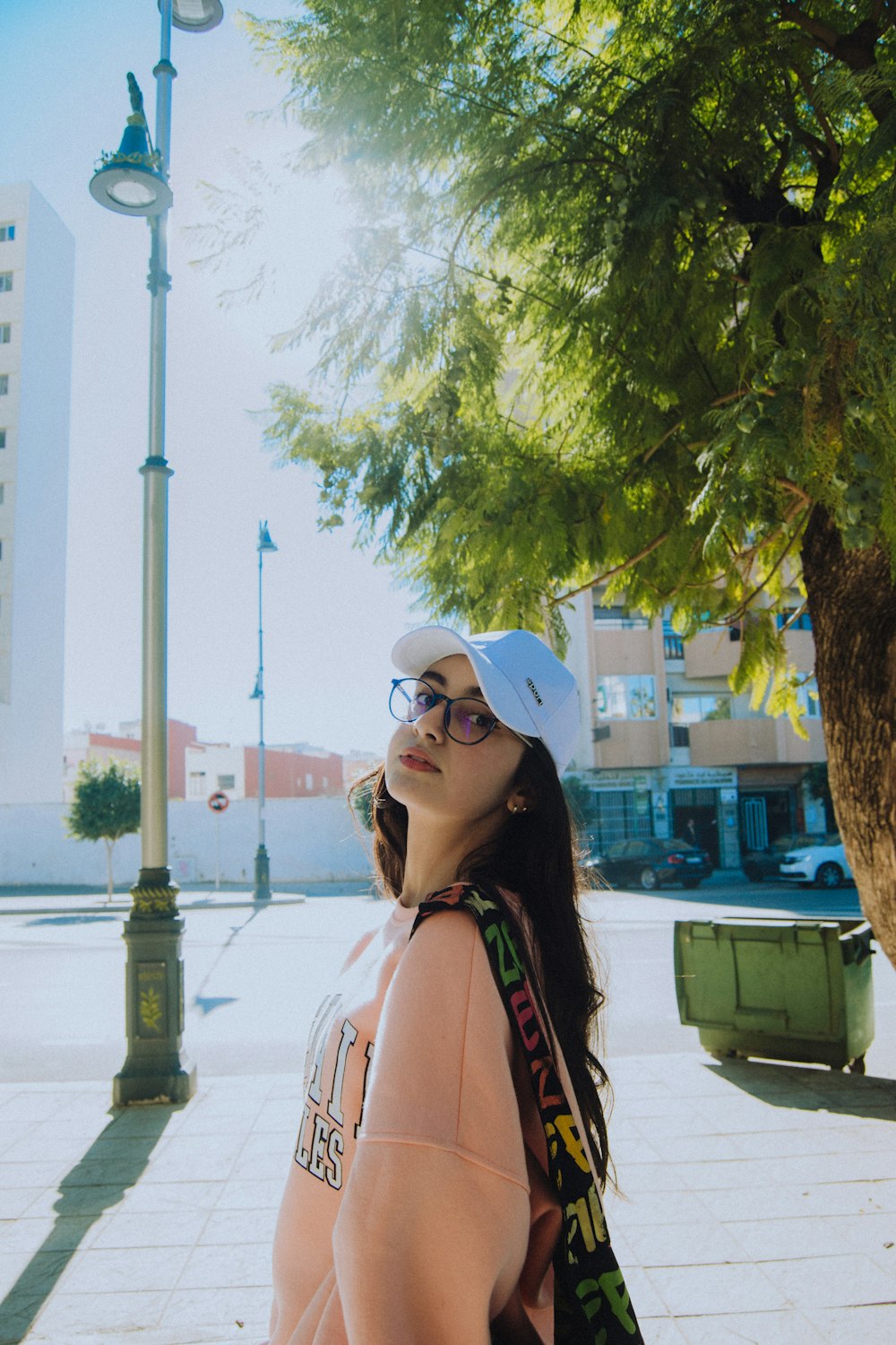 a woman wearing a hat and glasses standing under a tree