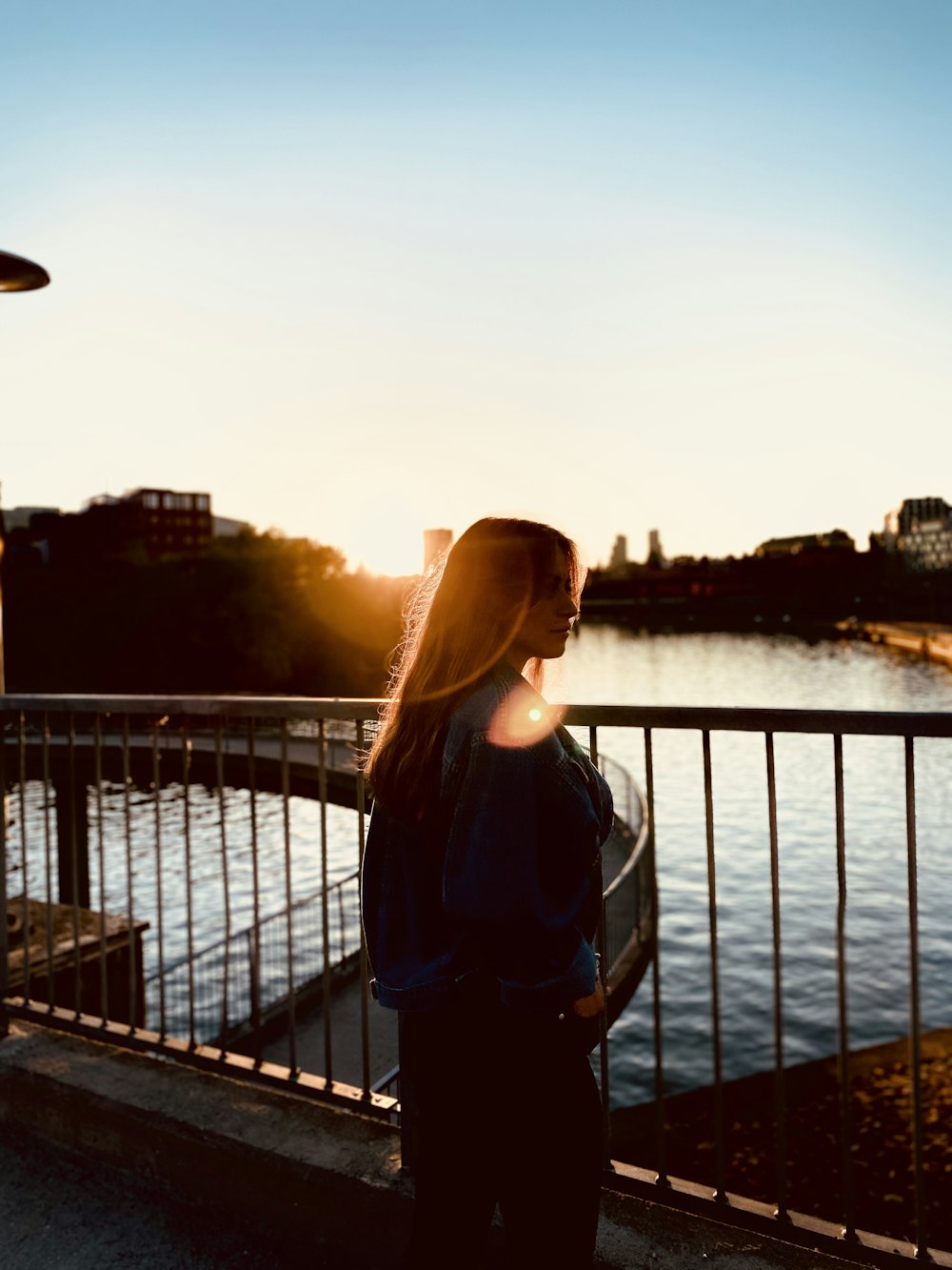 a woman standing next to a metal fence near a body of water