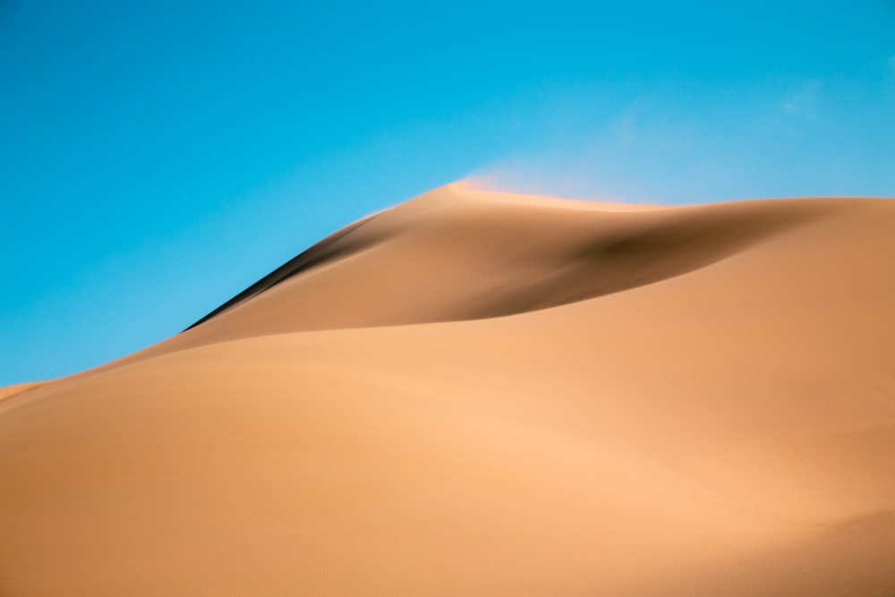 uma grande duna de areia com um céu azul no fundo