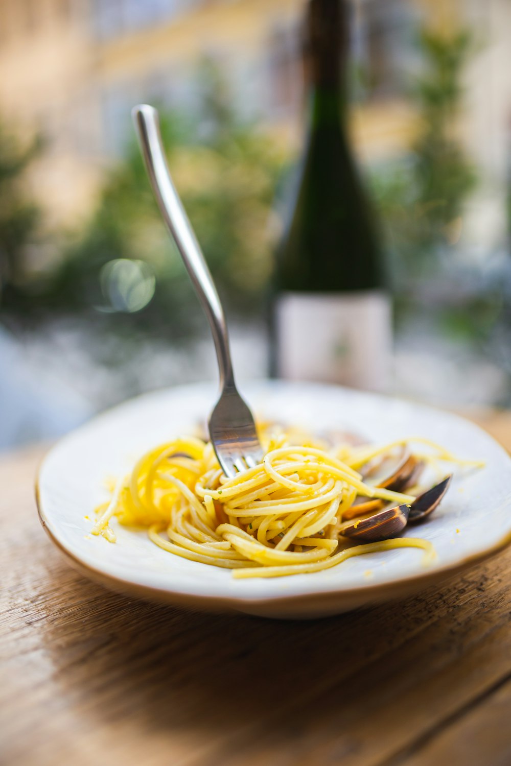 a plate of spaghetti with a bottle of wine in the background