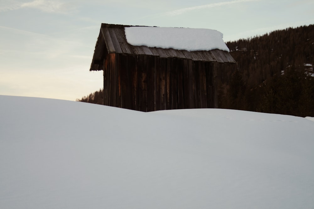 a snow covered hill with a small cabin in the background