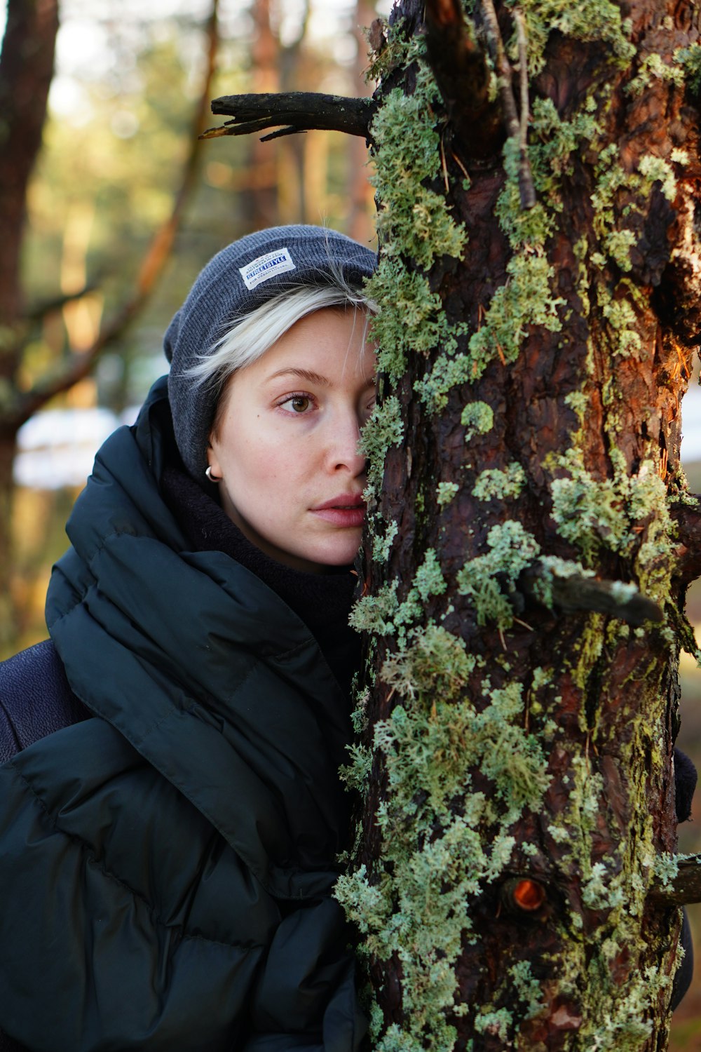 a woman standing next to a tree covered in green moss