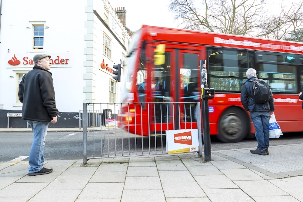 a group of people standing on a sidewalk next to a red bus