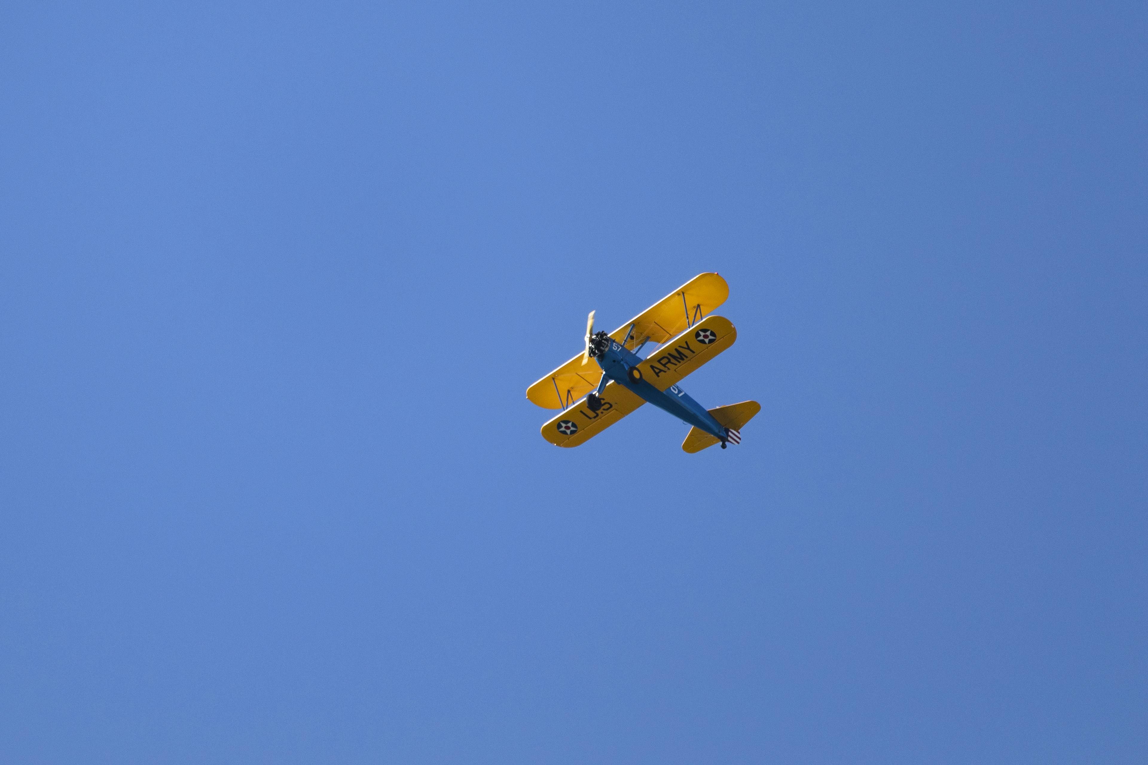a small yellow airplane flying through a blue sky