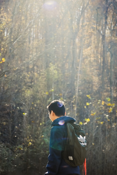 A person wearing a lightweight, breathable outdoor jacket standing on a forest trail at sunrise.