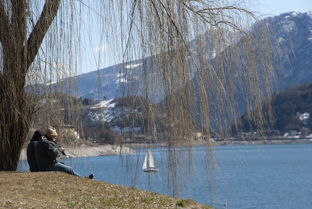 a man sitting on a hill next to a lake