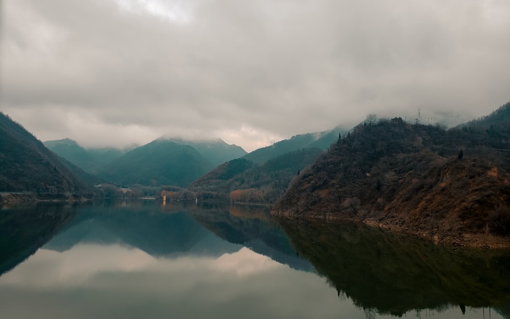 a body of water surrounded by mountains under a cloudy sky