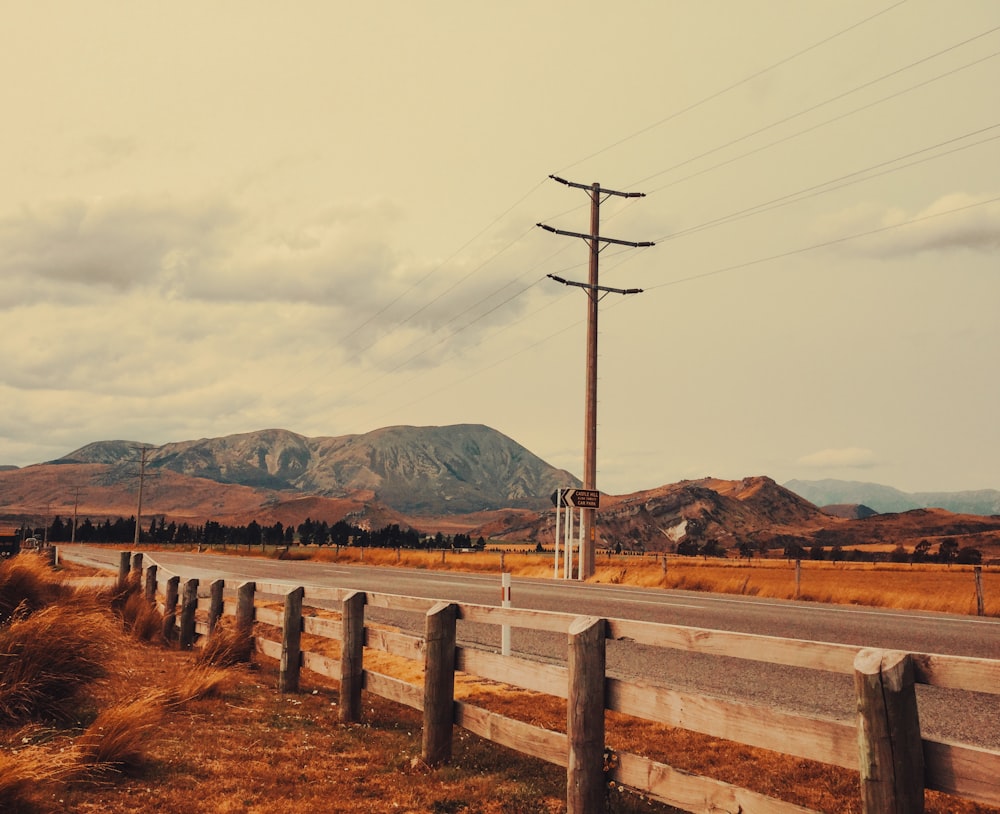 a wooden fence along a road with mountains in the background